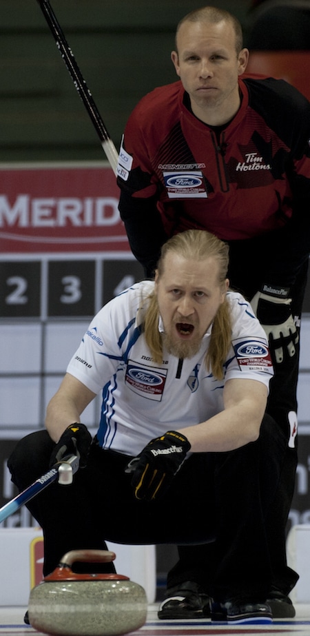 Aku Kauste de la Finlande appelle à ses balayeuses, comme Pat Simmons du Canada regarde par dessus son épaule. (Photo, Curling Canada / Michael Burns)