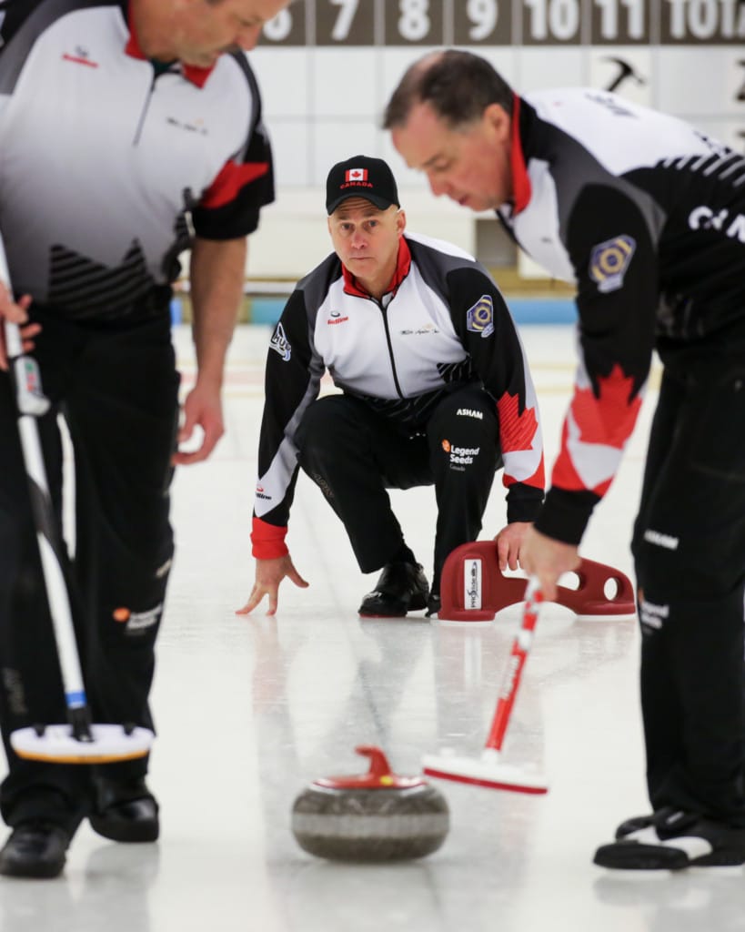 Le skip canadien Randy Neufeld observe son lancer alors que les balayeurs Peter Nicholls, à gauche, et Dale Michie contrôlent la pesanteur, durant leur match de samedi contre la Slovaquie, une victoire 8-2 pour le Canada. (Photo, Fédération mondiale de curling/Céline Stucki)