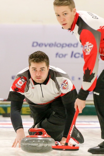 Team Canada lead Rob Gordon prepares to sweep skip Matt Dunstone’s rock during action against Switzerland at the 2016 World Junior Curling Championships (WCF/Richar Gray photo)